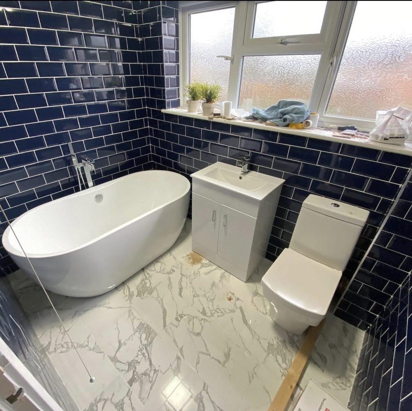 Navy metro tiled bathroom with freestanding bath and marble effect floor fitted in Leeds